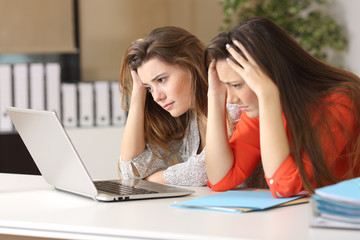 Sad coworkers watching content in a laptop