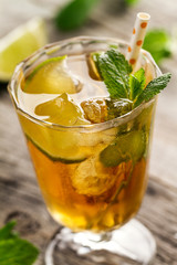Tasty fresh refreshing summer tea drink with ice, cold tea, lime and mint in glass on wooden background. Closeup.
