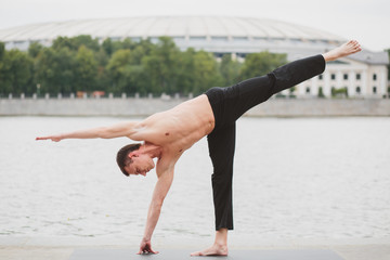 a young man practicing yoga asanas in the city on the waterfront