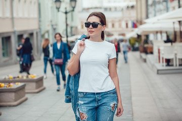 Fototapeta premium Attractive girl in sunglasses walking along the street. White t-shirt. Mock-up.