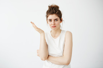 Displeased young beautiful girl with bun gesturing over white background.