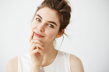 Fototapeta premium Portrait of young beautiful tender girl with bun smiling looking at camera touching face over white background. 