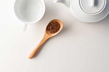 High angle view of white teapot and cup with wooden spoon of rooibos tea on table