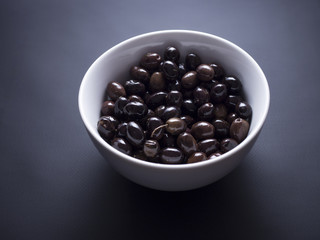 French black and brown niçoise olives in white bowl isolated on black background