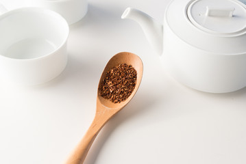 High angle close up view of wooden spoon with rooibos tea and white teapot and cup (selective focus)