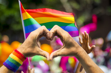 Hands making heart sign in front of rainbow flag - obrazy, fototapety, plakaty