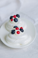 Close up of homemade individual meringue cakes Pavlova with mascarpone whipped cream garnished with fresh blueberries and red currants on a white stone background. Copy space.