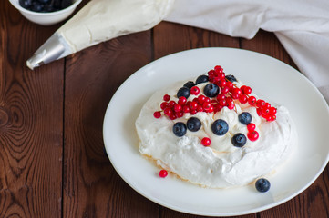 Close up of homemade individual meringue cakes Pavlova with whipped cream with mascarpone fresh blueberries and red currants in a white plate on a white stone background. Copy space.