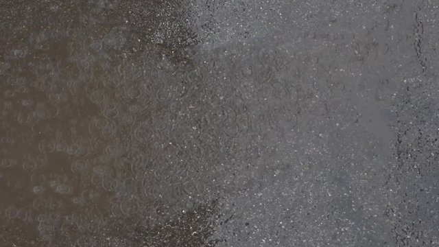 Panoramic top view of dark grey asphalt during rain. Puddles, waterdrops and circles on the water. Natural background. Rainy summer day.