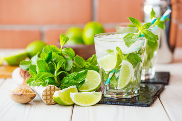 Two fresh mojitos cocktail in glass on wooden table. Mojitos with mint leaves, lime and ice. Drink making tools and ingredients for cocktail. 