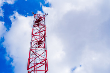 Mobile phone communication antenna tower with satellite dish on blue sky background with sun ray...