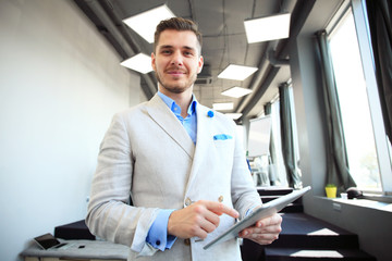 Fototapeta premium Working on new tablet. Low angle view of confident young man working on digital tablet while standing in front of the big window in office or cafe