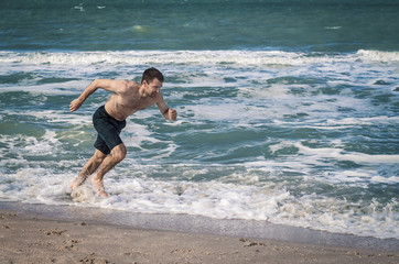 Fototapeta premium The guy is running at the beach close to the water