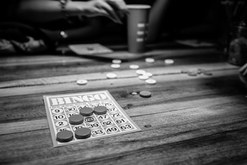Black and white photo of people playing bingo game and having very much fun of bingo game playing on a wooden table. Bingo card on the wooden table and the  game of chance is played.