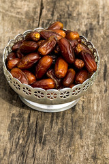 Dates fruit on a silver bowl on wooden table. The Muslim feast of the holy month of Ramadan Kareem