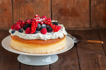 Close up of fluffy Japanese cotton cheesecake with wipped cream cheese frosting and garnished with forest berries served on a plate over wooden background.