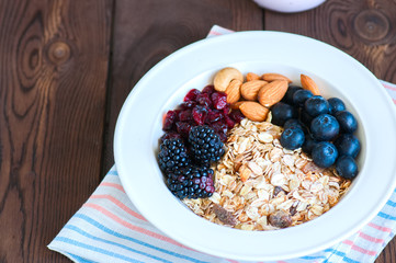 Healthy breakfast concept. Homemade muesli with blackberry, dry cranberry, blueberry, almond, yogurt in a jar, sour cream and milk on a wooden background. Close up and copy space.