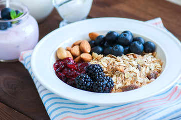 Healthy breakfast concept. Homemade muesli with blackberry, dry cranberry, blueberry, almond, yogurt in a jar, sour cream and milk on a wooden background. Close up and copy space.