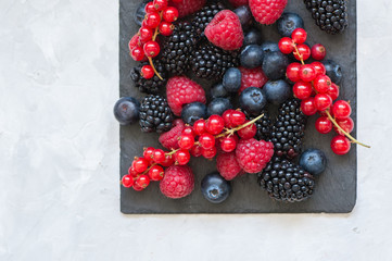  of berries raspberries red currants blueberries and blackberries on black slate board. White stone background.  Overhead view and copy space