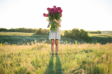 spectacular portrait of woman with big bouquet of rose peonies at sunset