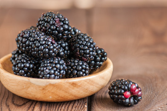 Close up of fresh ripe blackberries in a plate. Wooden background.