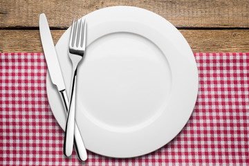 empty plate on a wooden background, a napkin in a red and white cage, a fork a knife