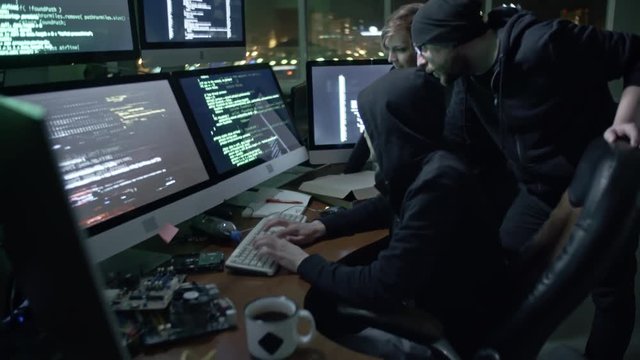 Tilt down of hackers cracking code in office at night. Two man and woman working together in team 