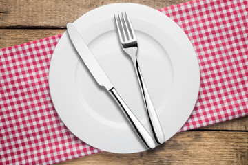 empty plate on a wooden background, a napkin in a red and white cage, a fork a knife