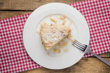 cake Napoleon on a white plate, on a wooden background and a red-white napkin