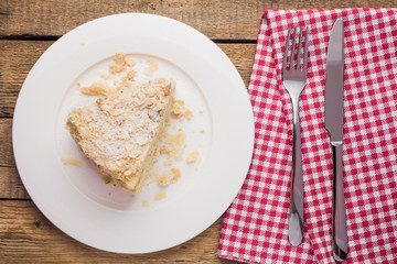 cake Napoleon on a white plate, on a wooden background and a red-white napkin