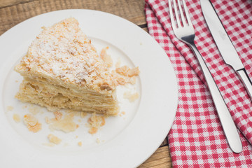 cake Napoleon on a white plate, on a wooden background and a red-white napkin
