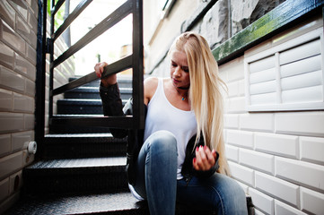 Obraz na płótnie Canvas Stylish blonde woman wear at jeans, choker and leather jacket at street near stairs. Fashion urban model portrait.