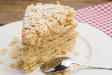 cake Napoleon on a white plate, on a wooden background and a red-white napkin