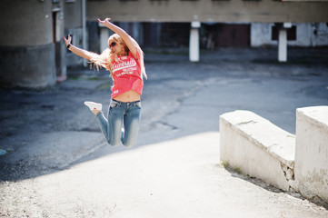 Obraz na płótnie Canvas Stylish happy blonde woman wear at jeans, sunglasses and t-shirt jumping at street at sunny weather. Fashion urban model portrait.