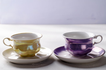 Empty colorful porcelain tableware. Yellow and violet cups on lilac background