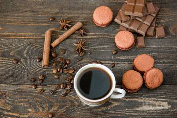 A cup of coffee with brown macaroons and chocolate on a wooden table