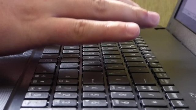 Caucasian man hands printing on laptop keyboard. Closeup view of computer with green wall behind. Office scene.