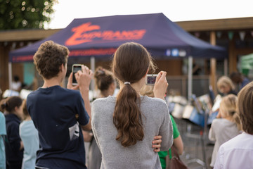Young boy and girl shoot a video of a music concert in a street on their mobile phone and camera....