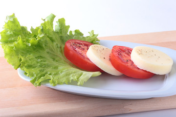 Portion of Mozzarella with Tomatoes, lettuce leaf and Balsamic dressing on white plate. selective focus close-up shot.