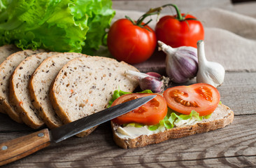 Sliced bread and a sandwich with tomatoes and salad on a wooden table. The concept of breakfast.
