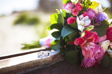 wedding rings and wedding bouquet lying on the wooden table

