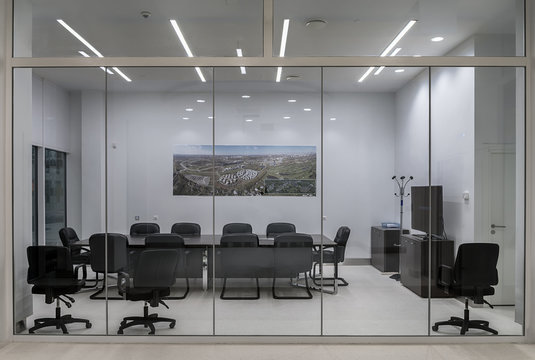 A modern meeting room with transparent partitions, with a large table and comfortable office chairs.
