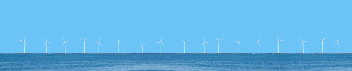 Wind power turbines, coastal placement, with blue sky and ocean.