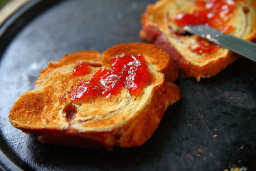 Spreading jam on brioche toast on a dark pan
