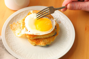 A man ready to cut into a fried egg on top of blueberry pancakes