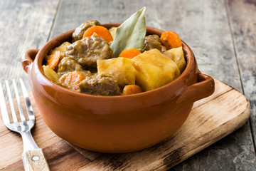 Beef meat stewed with potatoes, carrots and spices in ceramic bowl on wooden table
