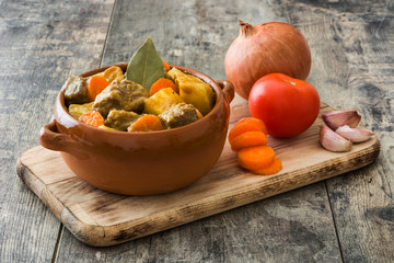 Beef meat stewed with potatoes, carrots and spices in ceramic bowl on wooden table
