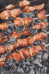 Pieces of tasty pork on skewers cooking on smoldering carbons outdoors