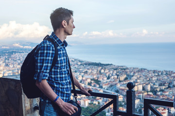 Man traveler with backpack explores the city looking at the panoramic view of the city and the coast.