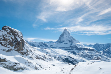 Scenic view on snowy Matterhorn peak in sunny day with blue sky and some clouds in background, Switzerland.